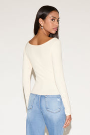 Woman wearing a cream long-sleeve top and light blue jeans on a white background