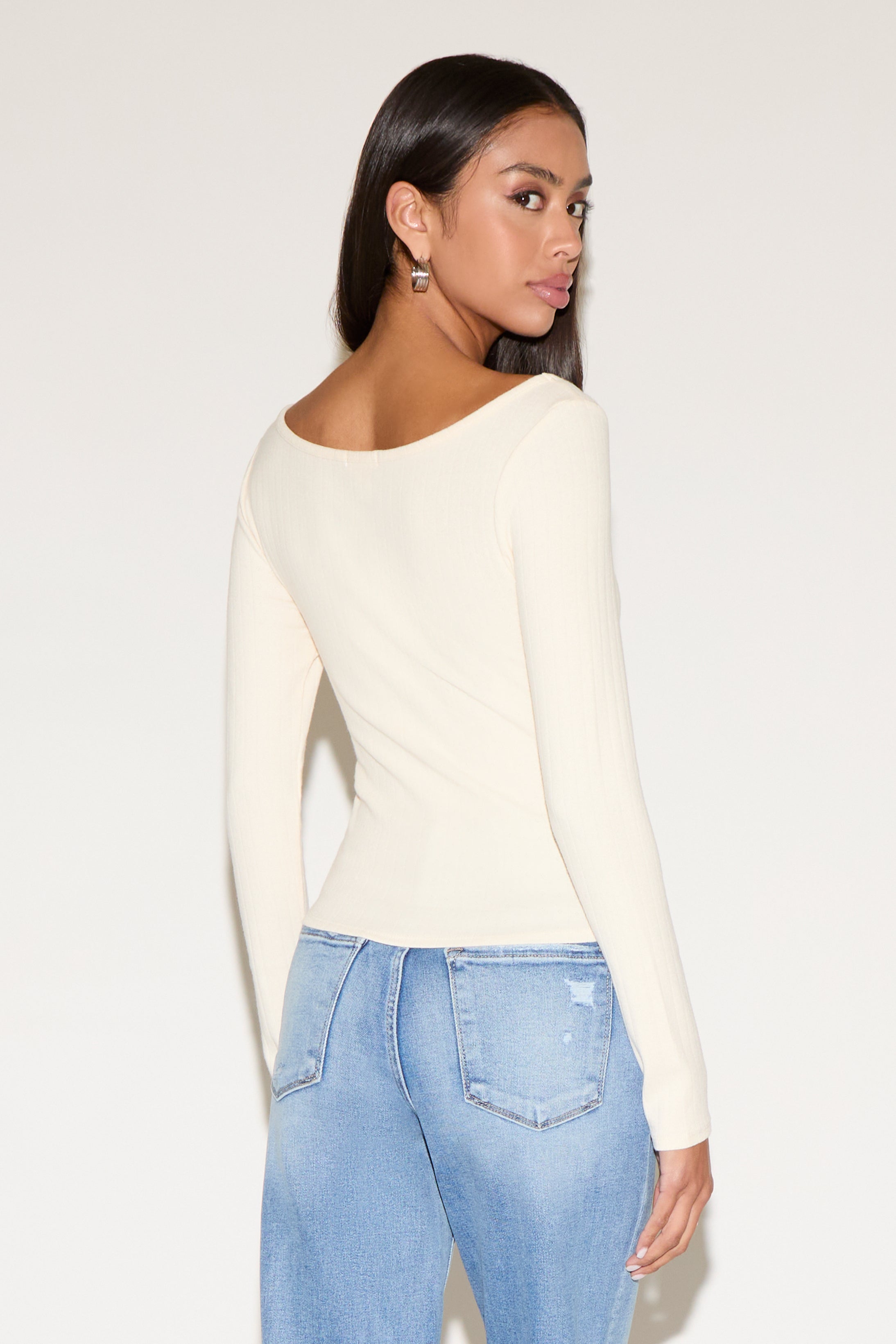 Woman wearing a cream long-sleeve top and light blue jeans on a white background