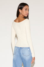 Woman wearing a cream long-sleeve top and light blue jeans on a white background