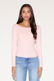 Woman wearing a light pink long-sleeve top and blue jeans on a white background