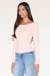 Woman wearing a pink long-sleeve top and blue jeans against a white background
