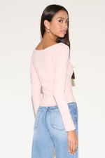 Woman wearing a light pink long-sleeve top and blue jeans on a white background