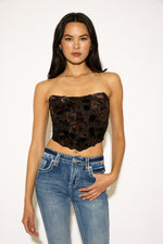 Woman wearing a black floral strapless top and blue jeans on a white background