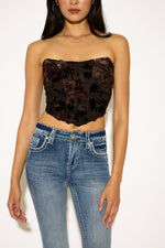 Woman wearing a black floral lace top and blue jeans on a white background