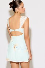 Woman wearing a light blue dress with floral design and cut-out back on a white background