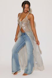 Woman wearing a sheer cover-up over denim pants on a white background