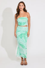 Model is wearing a green leaf print mesh tube top and flared maxi skirt set on a white background.
