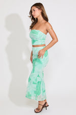 Model is wearing a green leaf print mesh tube top and flared maxi skirt set on a white background.