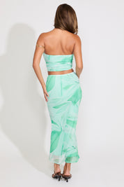 Model is wearing a green leaf print mesh tube top and flared maxi skirt set on a white background.