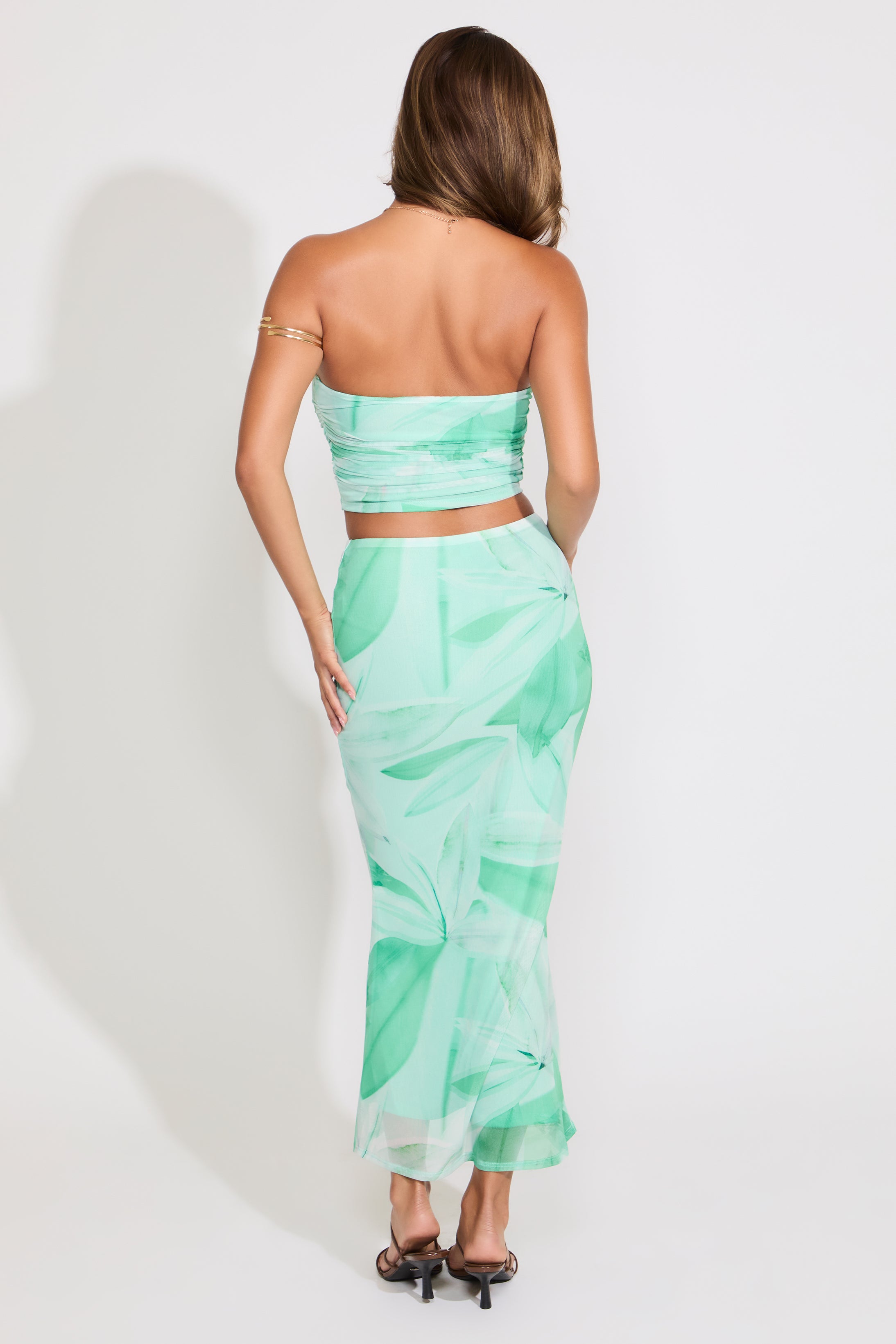 Model is wearing a green leaf print mesh tube top and flared maxi skirt set on a white background.