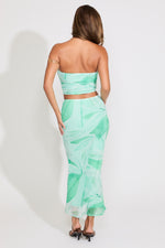 Model is wearing a green leaf print mesh tube top and flared maxi skirt set on a white background.