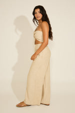 Woman in beige outfit standing against a plain background