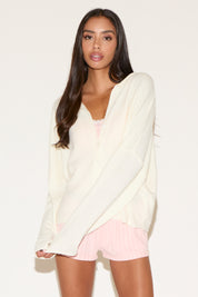 Woman wearing a white cardigan over a pink top and shorts on a beige background
