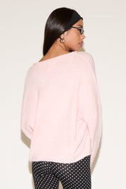 Person wearing a light pink sweater and black polka dot pants on a plain background