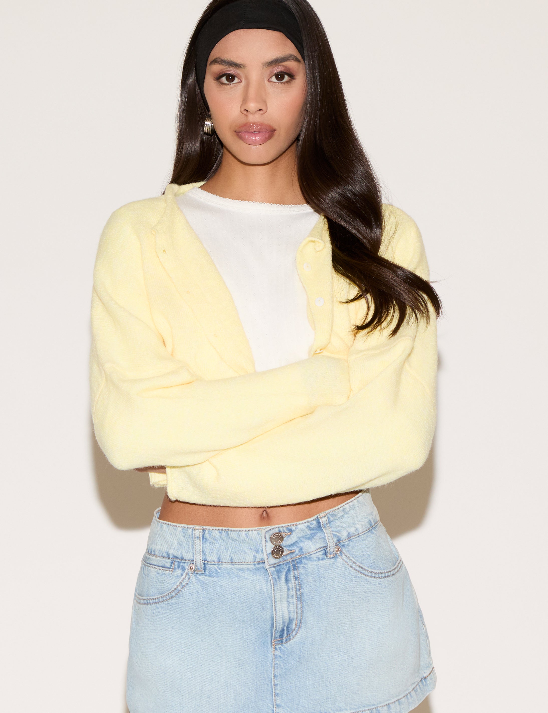 Woman wearing a yellow cardigan over a white shirt and denim skirt on a plain background