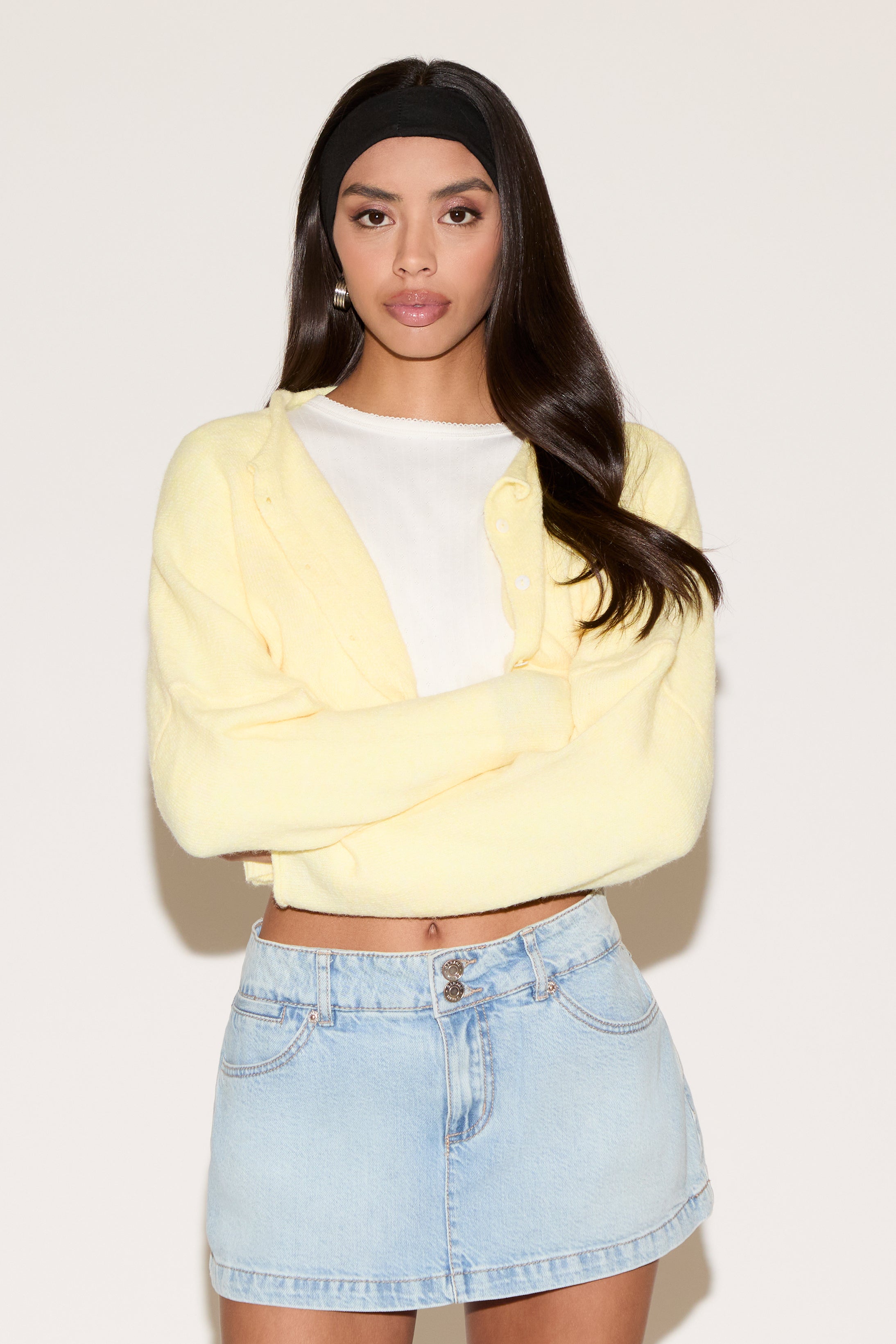 Woman wearing a yellow cardigan over a white shirt and denim skirt on a plain background