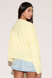 Woman wearing a light yellow sweater and denim skirt on a plain background