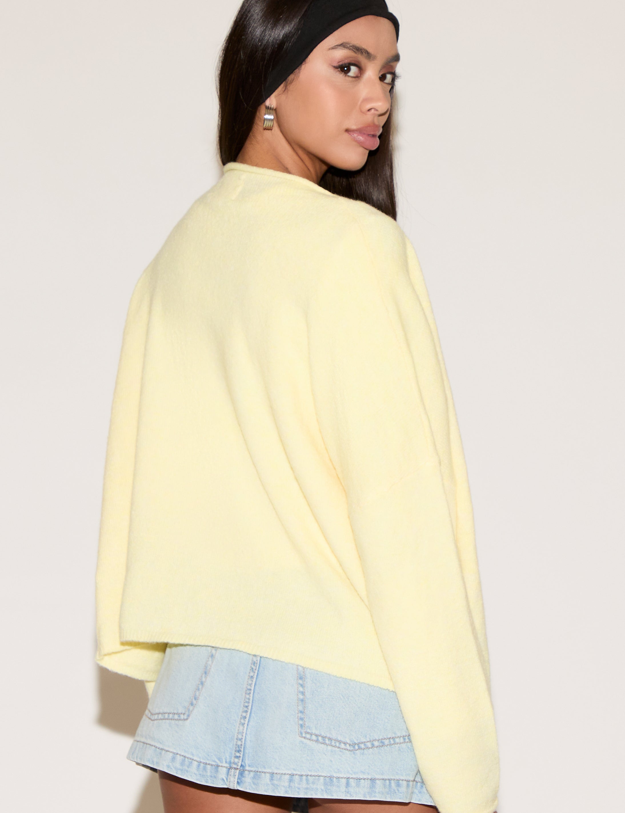Woman wearing a light yellow sweater and denim skirt on a plain background