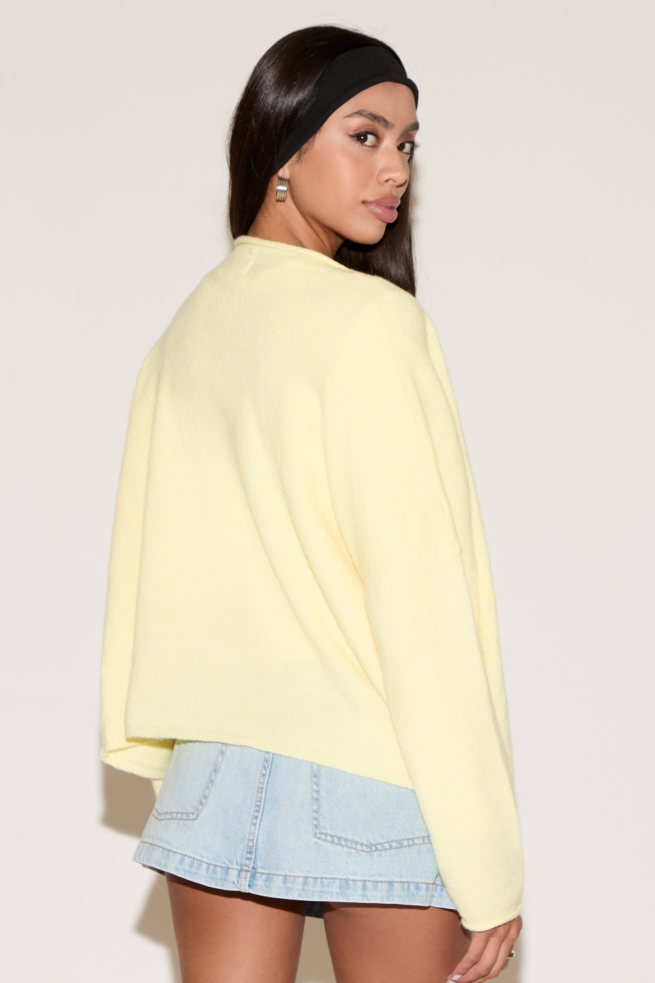 Woman wearing a light yellow sweater and denim skirt on a plain background
