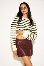 Woman wearing a striped sweater and leather skirt against a white background