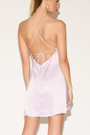 Woman wearing a light pink slip dress with thin straps on a white background