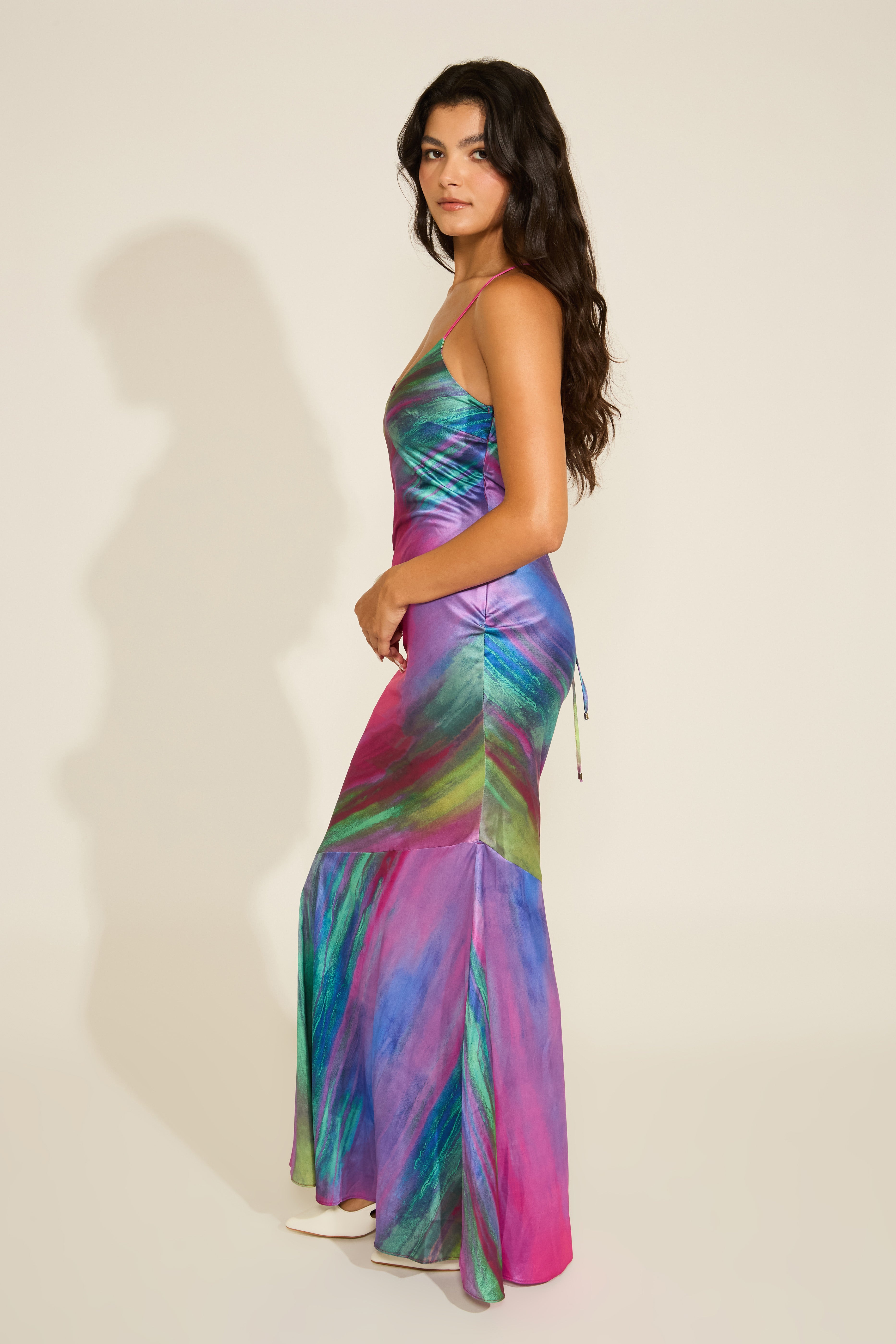 A woman wearing a sleeveless, maxi dress with a vibrant multi-color abstract print and a crisscross adjustable open back.