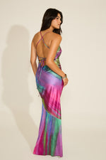 A woman wearing a sleeveless, maxi dress with a vibrant multi-color abstract print and a crisscross adjustable open back.