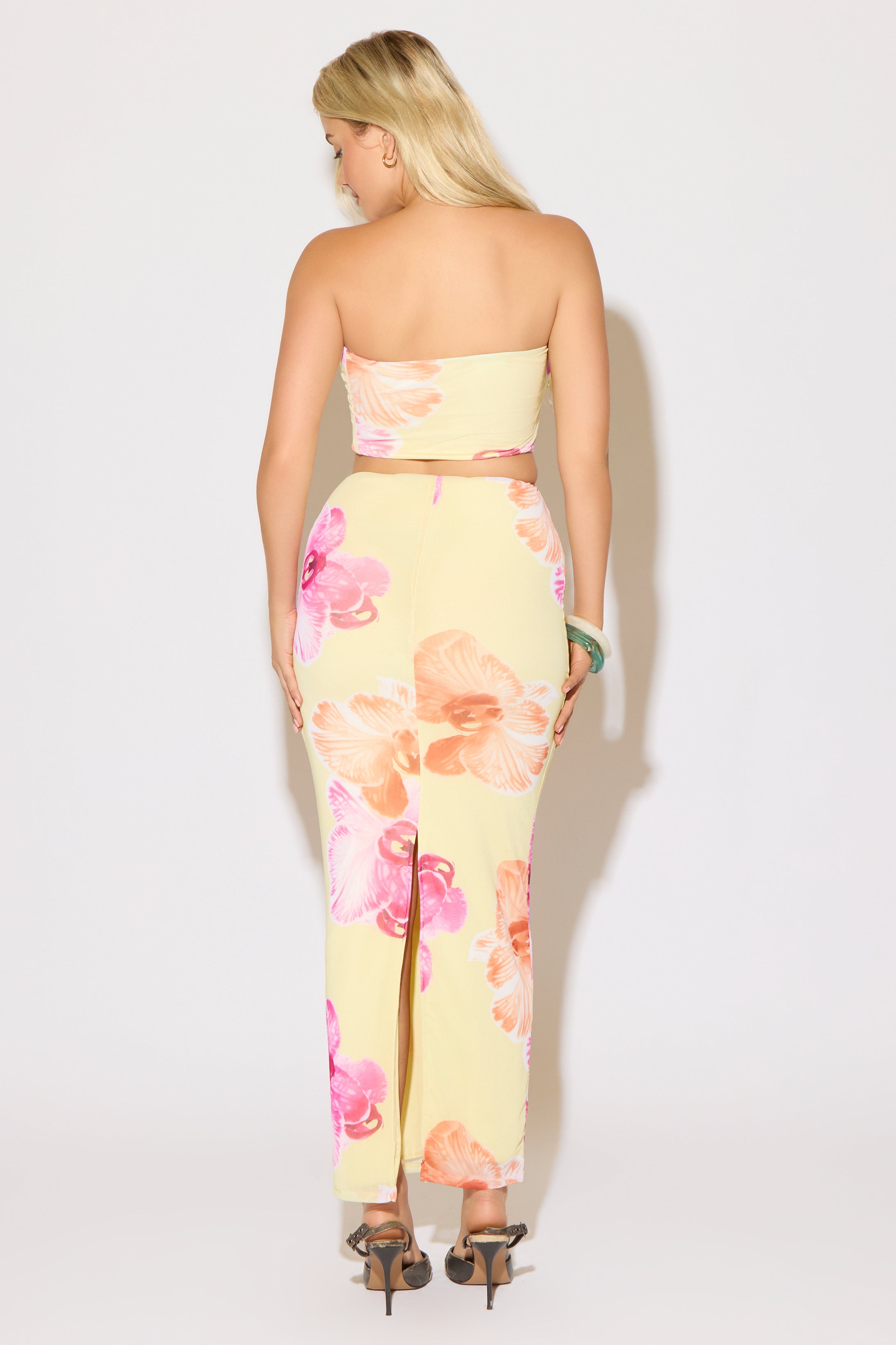 Model is wearing a yellow floral print crop tube top and maxi skirt set on a white background.