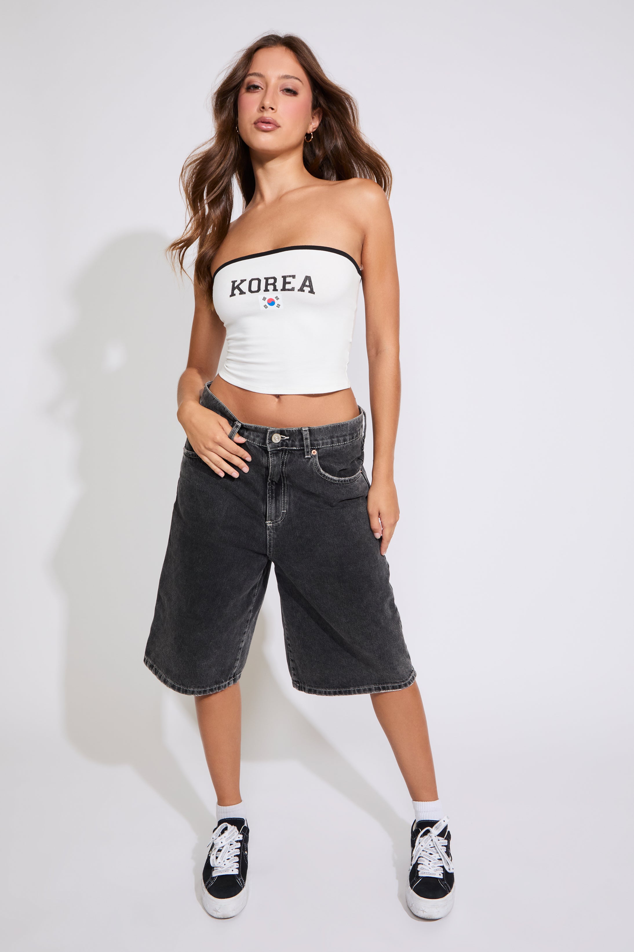 Model is wearing a white Korea logo strapless tube top with washed black denim jorts on a white background. 