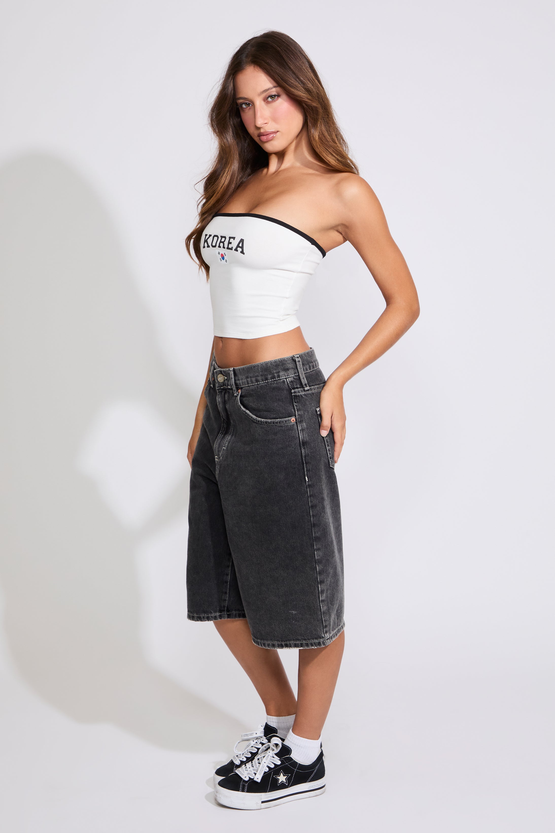 Model is wearing a white Korea logo strapless tube top with washed black denim jorts on a white background. 