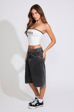 Model is wearing a white Korea logo strapless tube top with washed black denim jorts on a white background. 