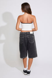 Model is wearing a white Korea logo strapless tube top with washed black denim jorts on a white background. 