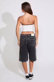 Model is wearing a white Mexico strapless tube top with washed black denim jorts on a white background. 
