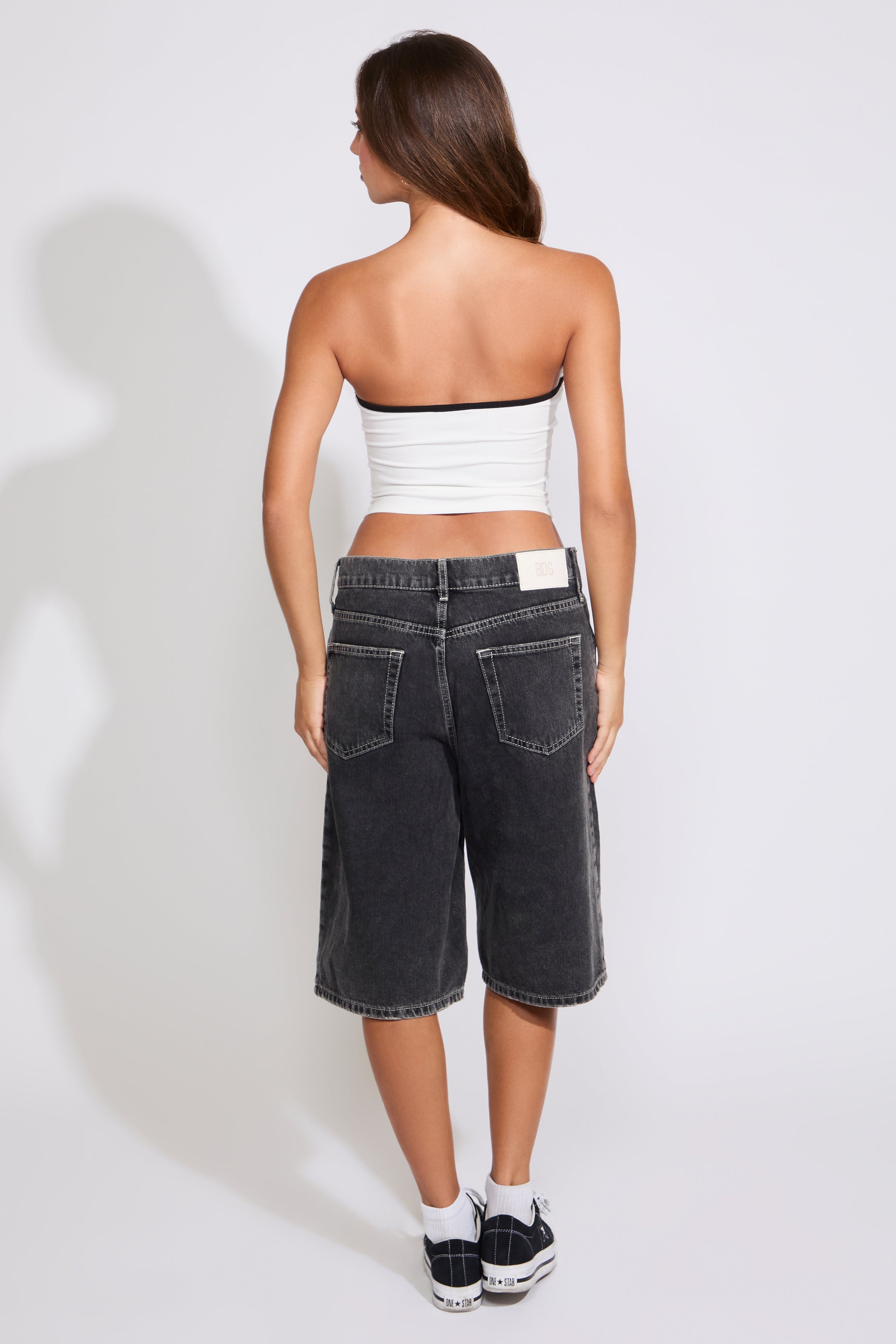 Model is wearing a white Mexico strapless tube top with washed black denim jorts on a white background. 