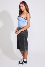 Model is wearing a blue USA strapless tube top with washed black denim jorts on a white background. 