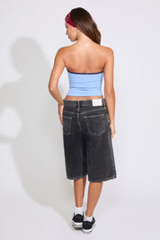 Model is wearing a blue USA strapless tube top with washed black denim jorts on a white background. 