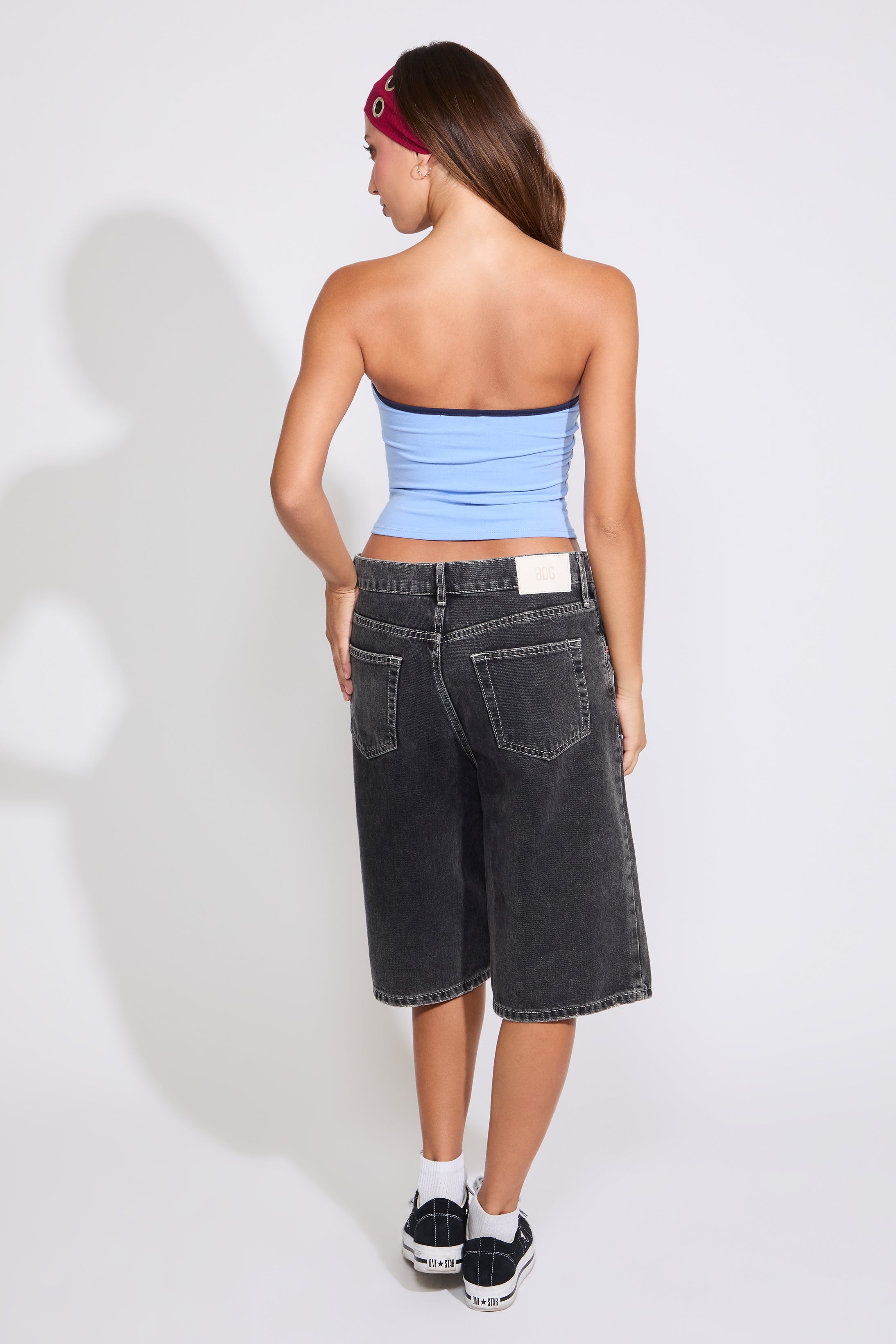 Model is wearing a blue USA strapless tube top with washed black denim jorts on a white background. 