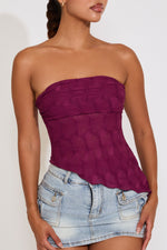 Woman wearing a strapless purple top and denim skirt on a white background