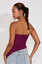 Woman wearing a strapless burgundy top and light blue jeans with a white background