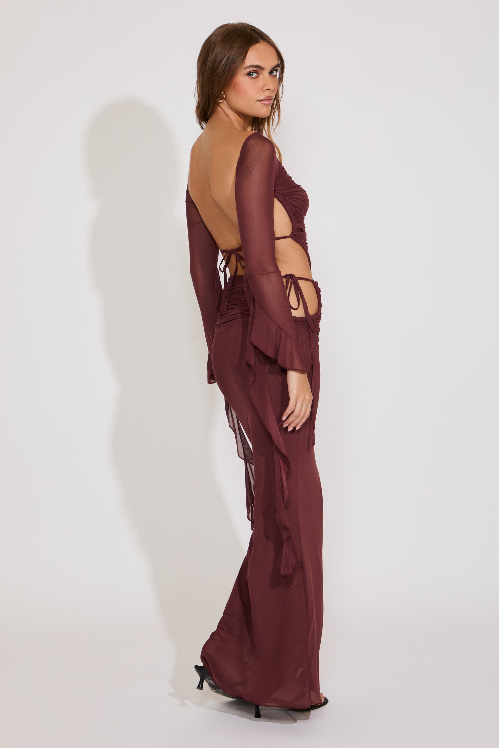 Woman wearing a burgundy outfit with sheer elements on a white background