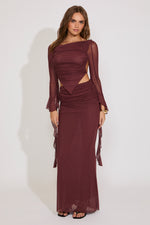 Woman wearing a burgundy evening gown with sheer sleeves against a white background