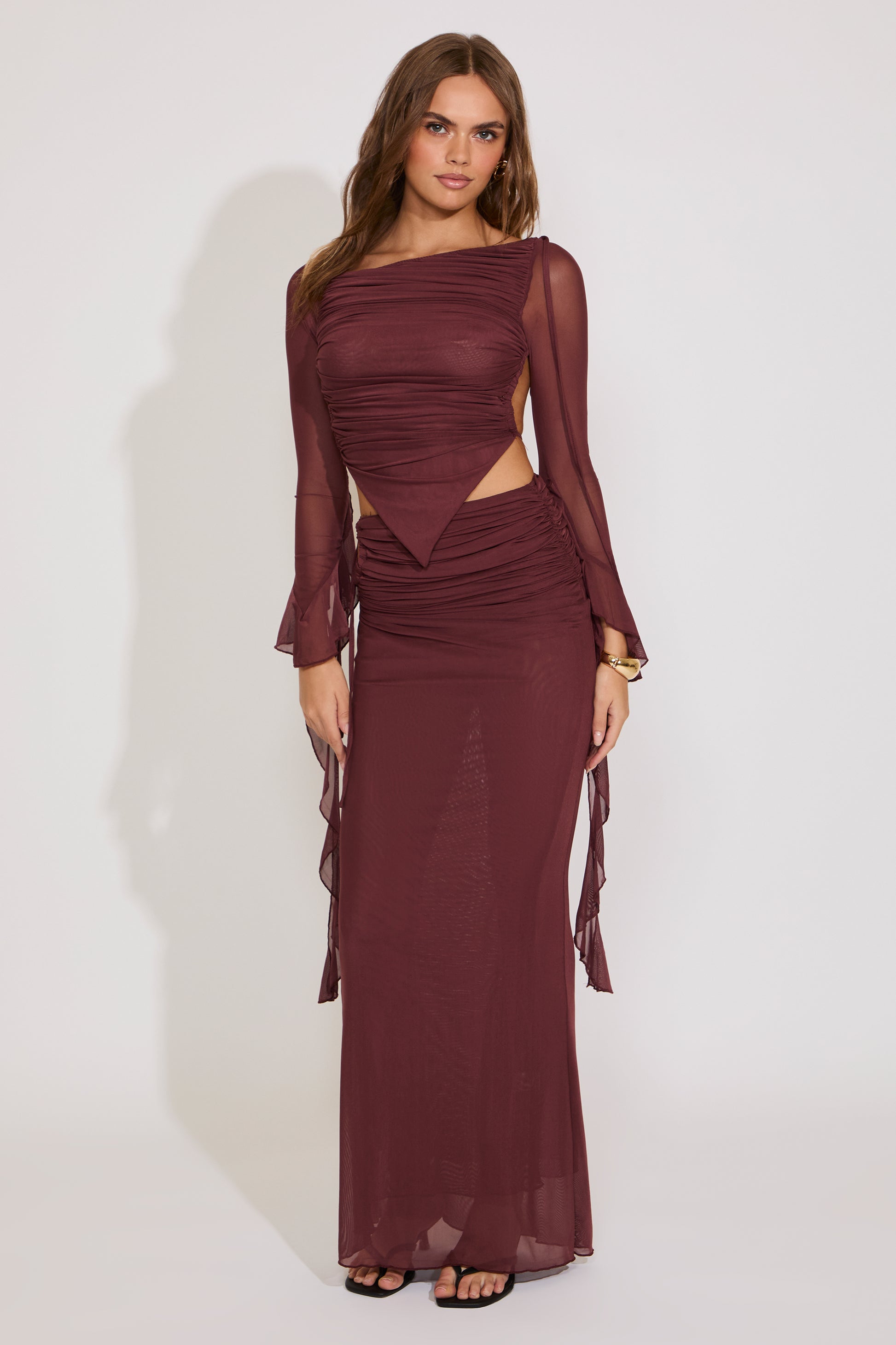 Woman wearing a burgundy evening gown with sheer sleeves against a white background