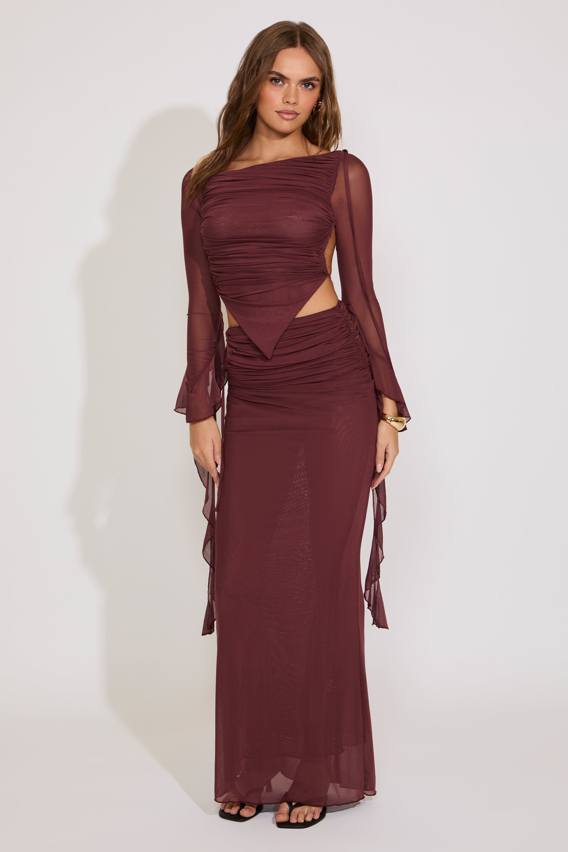 Woman wearing a burgundy evening gown with sheer sleeves against a white background