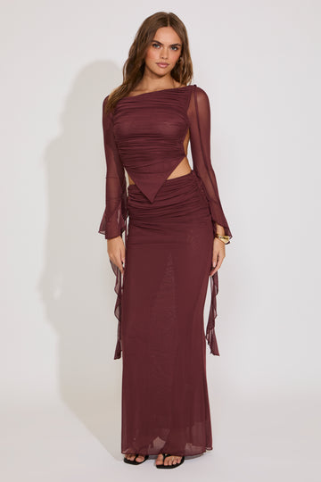 Woman wearing a burgundy evening gown with sheer sleeves against a white background