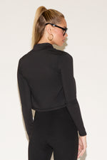 A woman wearing oversized sunglasses. She wears a black zip-up jacket and matching leggings. 