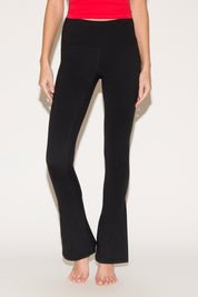 A person wearing black yoga pants and a red top stands barefoot on a light background.