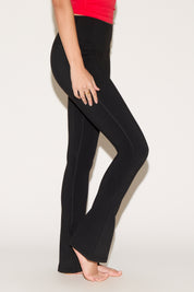 A person wearing black yoga pants and a red top stands barefoot on a light background.