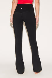 A person wearing black yoga pants and a red top stands barefoot on a light background.