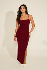 A model wearing a green sleeveless halter backless tie back side slit maxi dress with a cowl neckline.