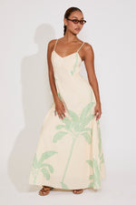 Woman wearing a cream dress with green palm leaf pattern against a white background
